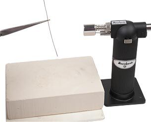Holding wire with tweezers next to firing block and torch